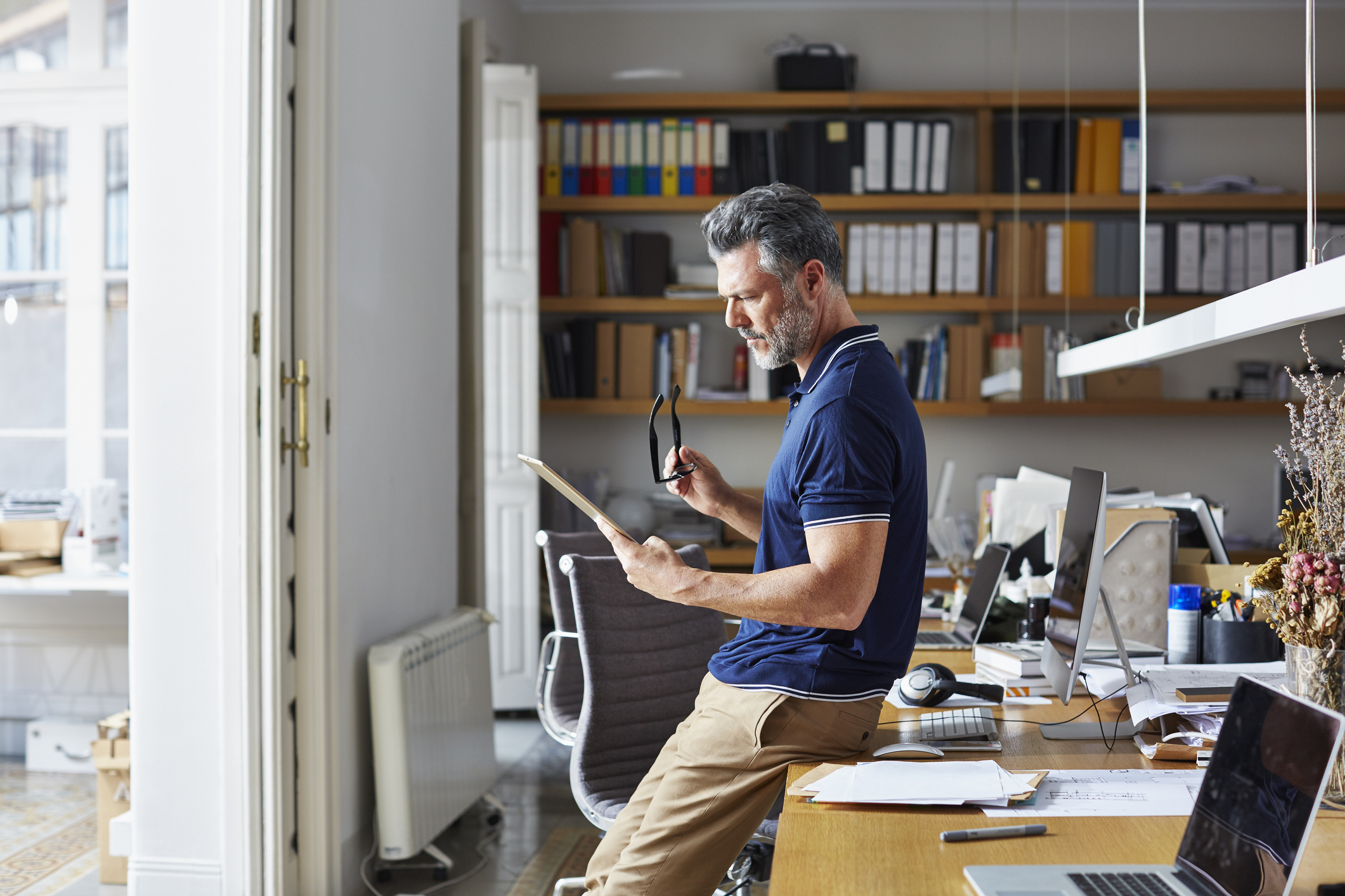 Side view of businessman using digital tablet while leaning on desk in office